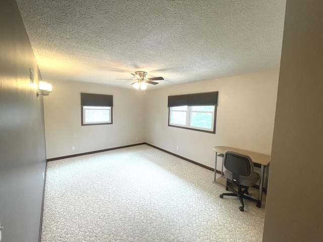 unfurnished office with carpet floors, a textured ceiling, ceiling fan, and plenty of natural light