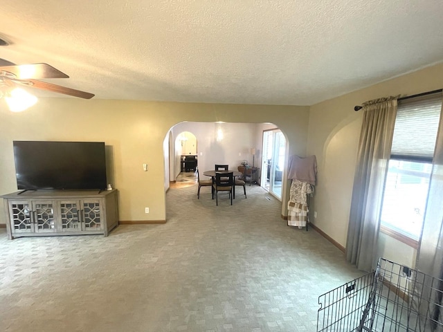 living area with arched walkways, a textured ceiling, carpet, a ceiling fan, and baseboards
