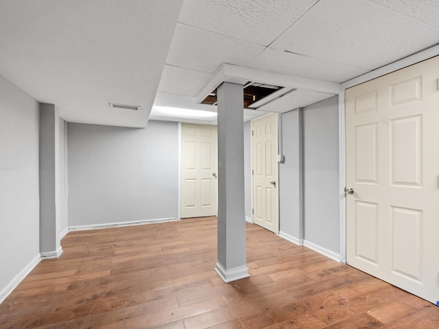 finished below grade area featuring a paneled ceiling, wood finished floors, baseboards, and visible vents