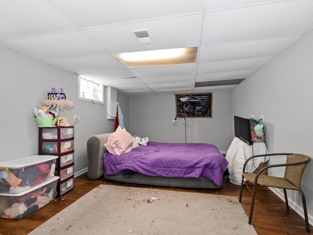 bedroom with visible vents, baseboards, a drop ceiling, and wood finished floors