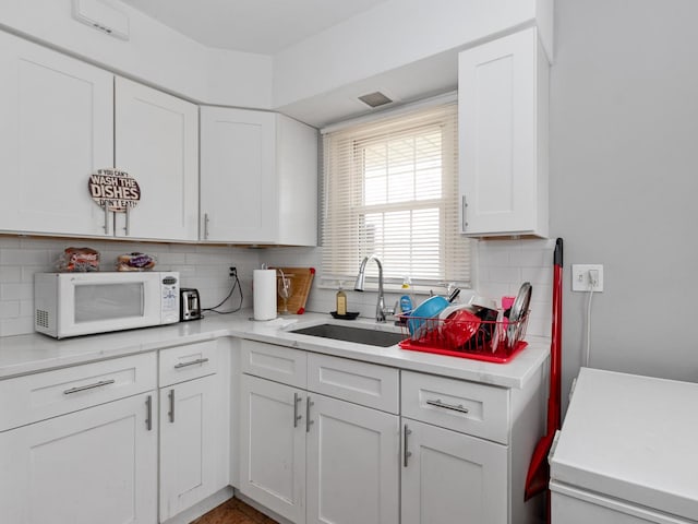 kitchen with white cabinets, white microwave, light countertops, and a sink
