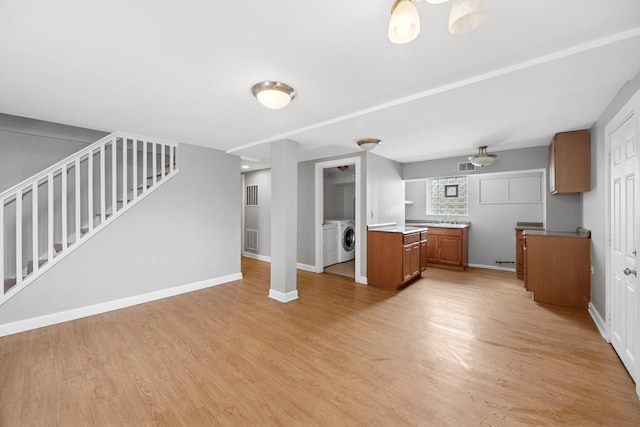 unfurnished living room with baseboards, washer and dryer, a sink, light wood-style floors, and stairs