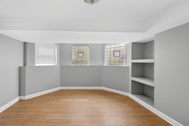 empty room with built in shelves, baseboards, and wood finished floors