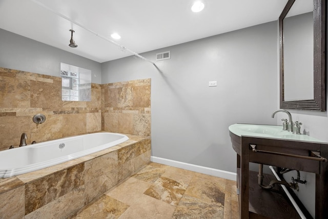 full bathroom featuring vanity, baseboards, stone finish floor, visible vents, and tiled tub