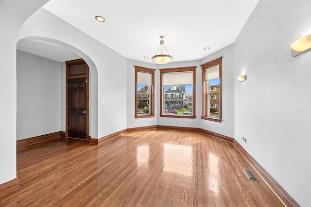 empty room with baseboards, recessed lighting, visible vents, arched walkways, and wood finished floors