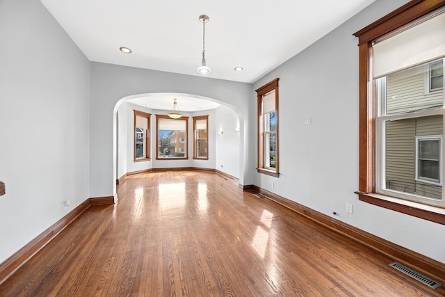 unfurnished room with arched walkways, visible vents, recessed lighting, wood finished floors, and baseboards