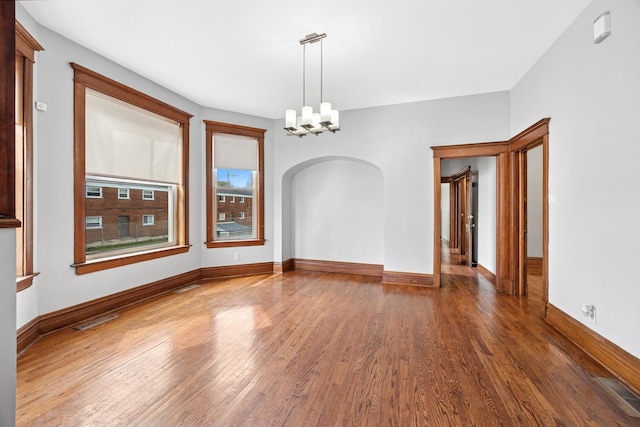 spare room with an inviting chandelier, arched walkways, visible vents, wood finished floors, and baseboards
