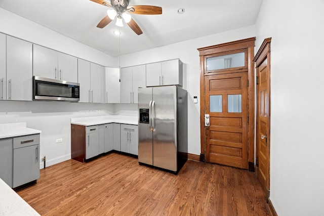 kitchen with gray cabinets, light wood-type flooring, appliances with stainless steel finishes, and a ceiling fan