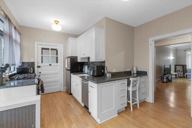 kitchen with backsplash, white cabinets, appliances with stainless steel finishes, and light wood-style floors