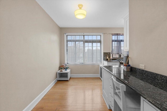 kitchen with white cabinets, baseboards, dark stone counters, light wood-style flooring, and beverage cooler