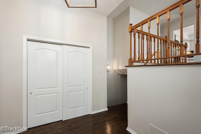 hallway featuring dark wood finished floors, baseboards, and a high ceiling