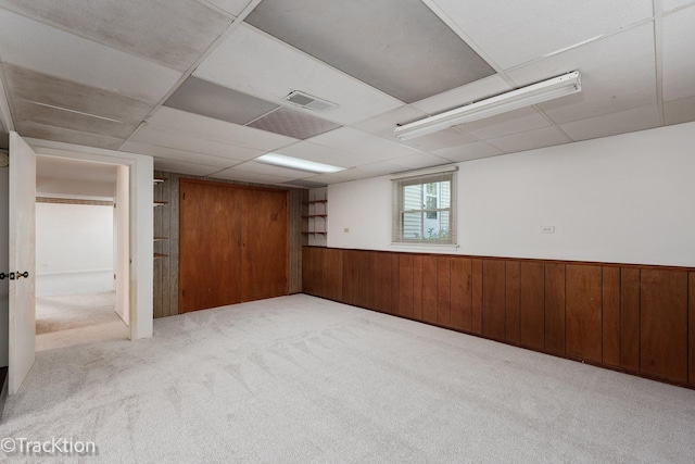 basement featuring carpet, wooden walls, wainscoting, and a drop ceiling