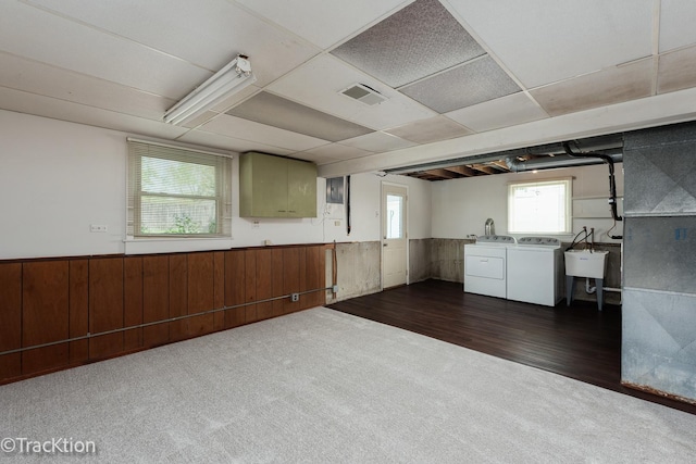 below grade area featuring washing machine and dryer, dark carpet, wainscoting, dark wood-style floors, and a sink