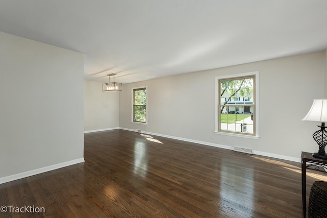 unfurnished living room featuring plenty of natural light, dark wood-type flooring, and a chandelier