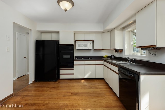 kitchen with black appliances, a sink, dark countertops, a warming drawer, and light wood finished floors