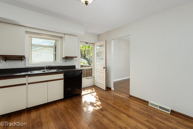 kitchen with dishwasher, dark countertops, a sink, and white cabinetry