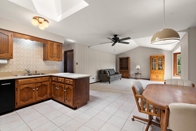 kitchen with a sink, vaulted ceiling with skylight, light countertops, black dishwasher, and a peninsula