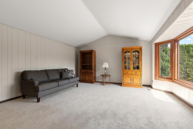 living area with wooden walls, carpet, and lofted ceiling
