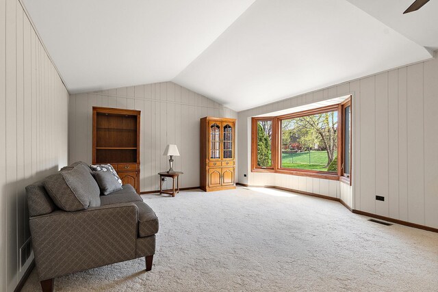 sitting room featuring wooden walls, carpet, vaulted ceiling, and visible vents