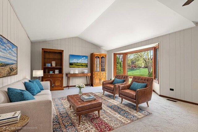 living room with vaulted ceiling, wood walls, and light colored carpet