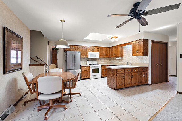 kitchen with brown cabinetry, visible vents, a skylight, light countertops, and white appliances