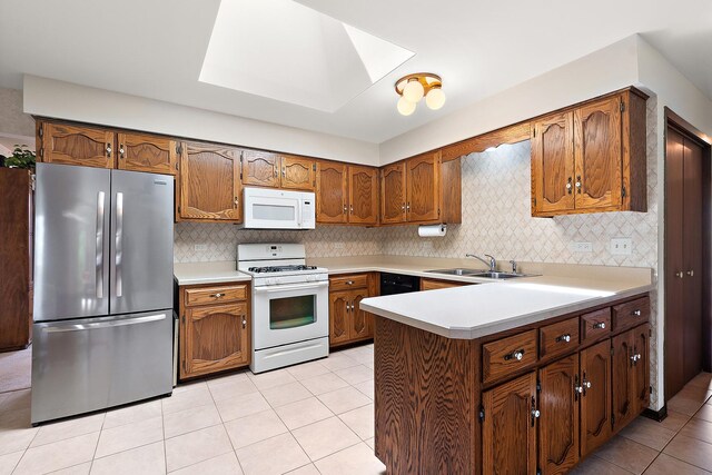 kitchen with a sink, white appliances, brown cabinetry, light tile patterned floors, and a skylight