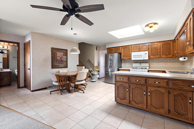 kitchen with brown cabinetry, white appliances, light countertops, a sink, and a skylight
