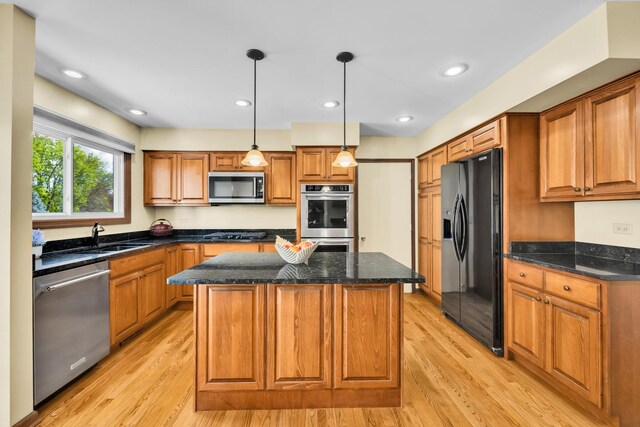 kitchen featuring appliances with stainless steel finishes, a sink, light wood-type flooring, a kitchen island, and brown cabinetry