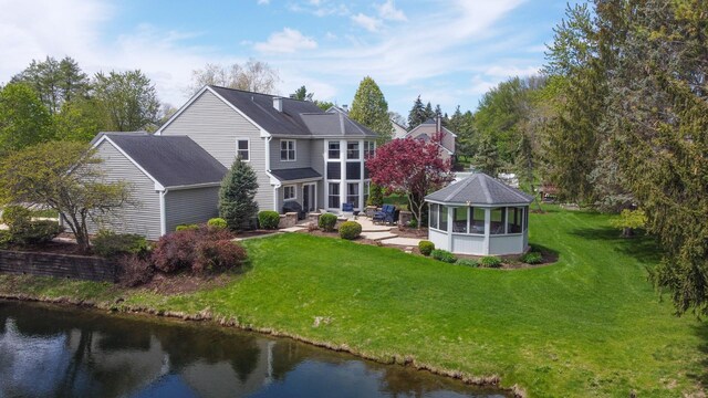 back of house featuring a patio, a sunroom, a lawn, and a water view