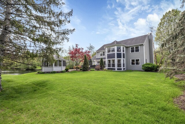 rear view of property with a yard, a sunroom, a chimney, and a water view