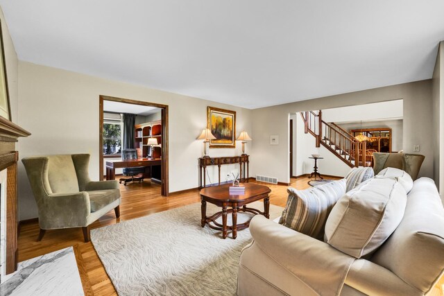 living area featuring stairway, a desk, a fireplace, light wood-type flooring, and baseboards