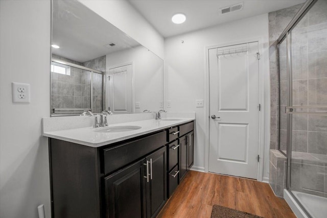 bathroom with double vanity, a stall shower, visible vents, a sink, and wood finished floors