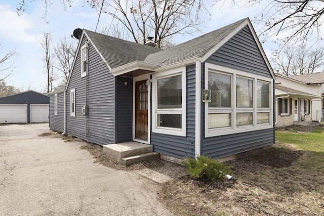 view of front of home featuring an outbuilding, a chimney, a garage, and roof with shingles