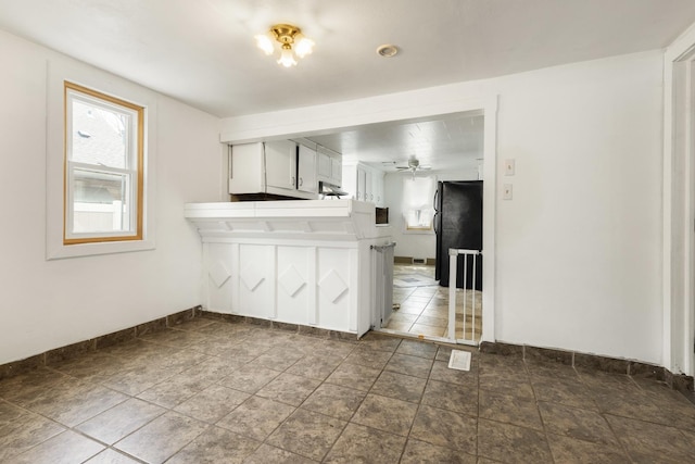 kitchen featuring baseboards, ceiling fan, freestanding refrigerator, stone finish floor, and white cabinetry
