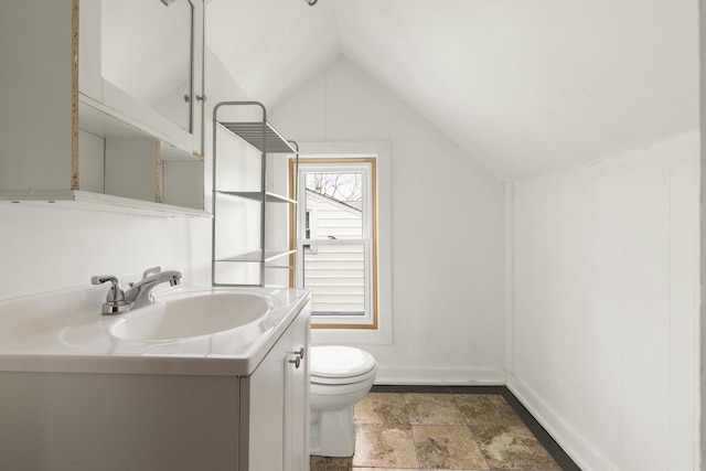 bathroom featuring stone finish floor, vanity, toilet, lofted ceiling, and baseboards
