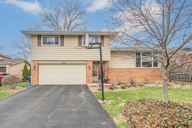 split level home featuring a garage, a front lawn, fence, brick siding, and driveway
