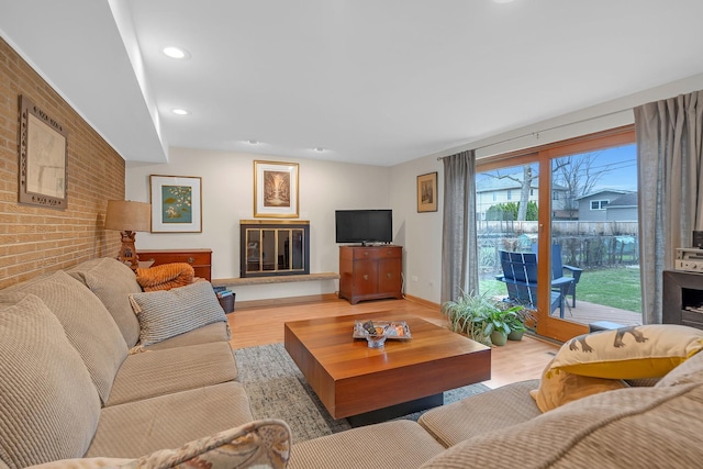 living room featuring recessed lighting, baseboards, light wood finished floors, and brick wall