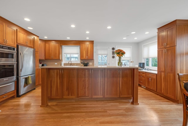 kitchen with appliances with stainless steel finishes, brown cabinets, light wood-type flooring, light countertops, and a warming drawer