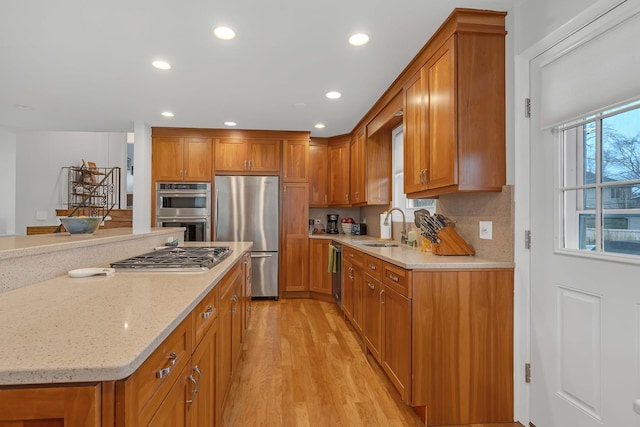 kitchen with a sink, appliances with stainless steel finishes, light wood-type flooring, and brown cabinets