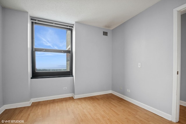 empty room with visible vents, baseboards, wood finished floors, and a healthy amount of sunlight