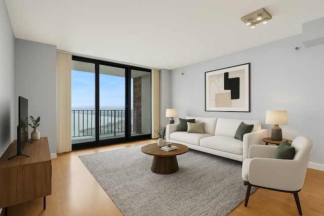 living room featuring a water view, baseboards, light wood finished floors, and floor to ceiling windows