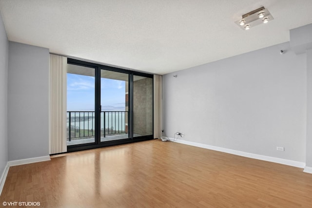 unfurnished room featuring expansive windows, baseboards, and wood finished floors