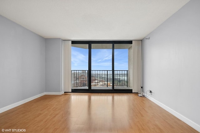 empty room featuring expansive windows, baseboards, and wood finished floors