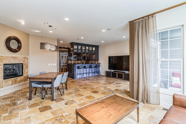 dining room featuring a tiled fireplace, stone tile flooring, visible vents, and recessed lighting