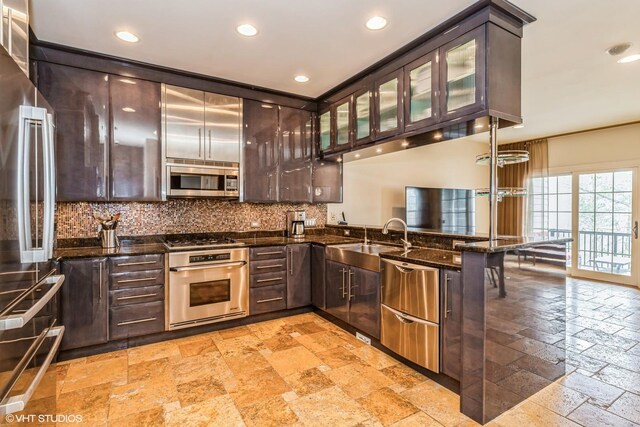 kitchen with stainless steel appliances, a sink, stone tile flooring, dark brown cabinetry, and a peninsula