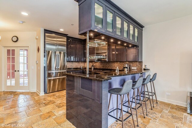 kitchen featuring stone tile floors, high quality fridge, dark stone counters, and tasteful backsplash