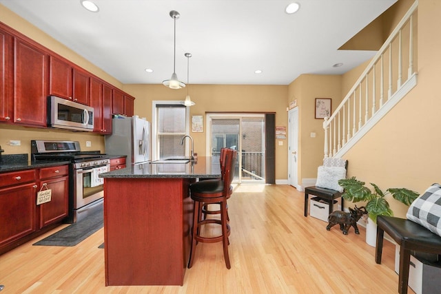kitchen with reddish brown cabinets, a sink, light wood-style flooring, and stainless steel appliances