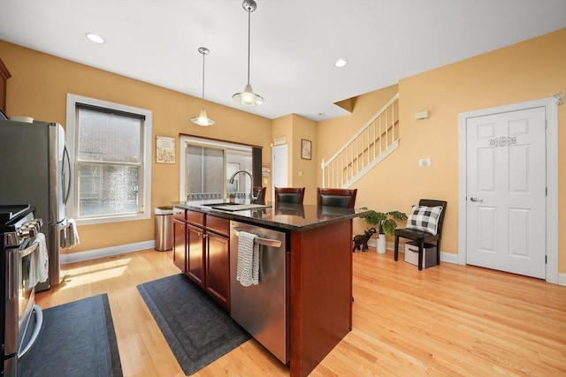 kitchen featuring a kitchen island with sink, baseboards, a sink, light wood finished floors, and appliances with stainless steel finishes