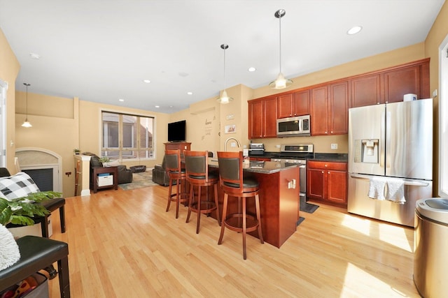 kitchen with dark countertops, stainless steel appliances, open floor plan, light wood-type flooring, and a kitchen bar