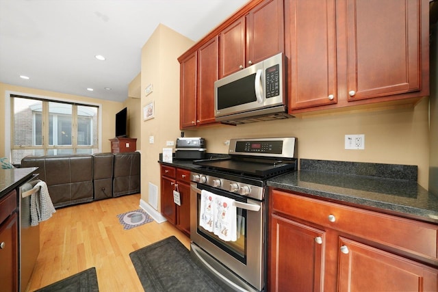 kitchen featuring appliances with stainless steel finishes, dark stone countertops, recessed lighting, open floor plan, and light wood-type flooring